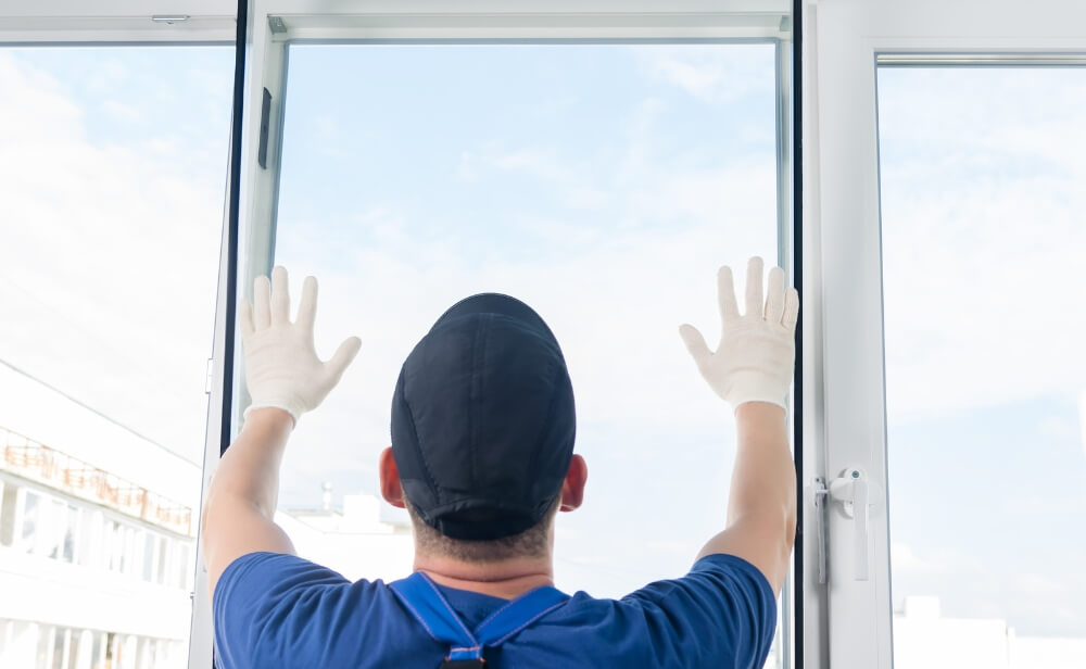 Reparatii ferestre termopan o persoana care repara o fereastra de termopan cu avand manusi in mana