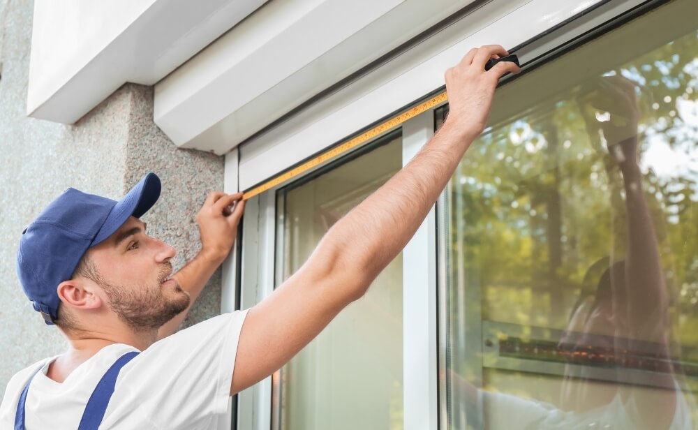 Producem rulouri exterioare o persoana care masoara un geam pentru montarea de rulouri exterioare